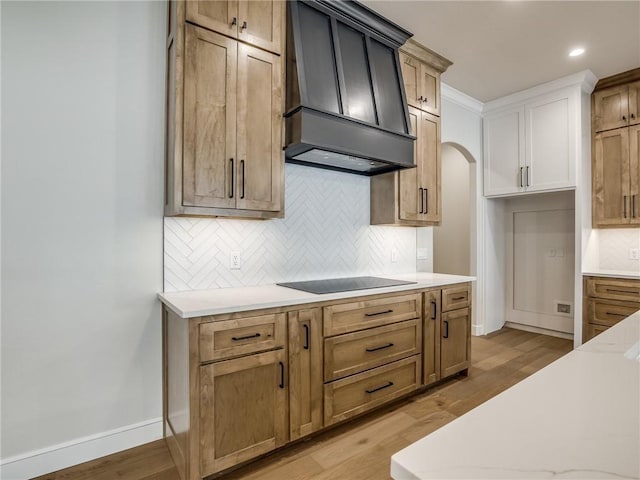 kitchen featuring light countertops, light wood-style floors, premium range hood, and black electric stovetop