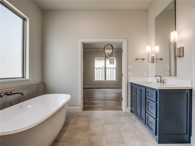 full bath with vanity, baseboards, a soaking tub, a chandelier, and tile patterned flooring