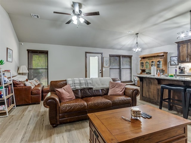 living area with light wood-style flooring, ceiling fan with notable chandelier, visible vents, and vaulted ceiling