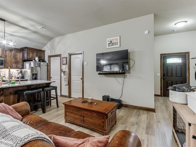 living area with light wood-type flooring, baseboards, vaulted ceiling, and visible vents