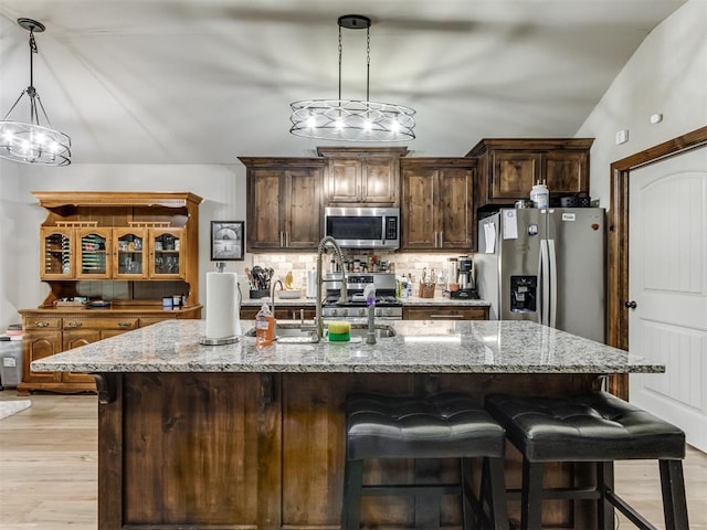 kitchen featuring tasteful backsplash, light wood-style flooring, light stone countertops, a kitchen bar, and appliances with stainless steel finishes