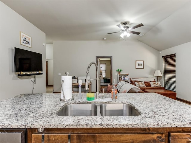 kitchen with open floor plan, a sink, a ceiling fan, and light stone counters