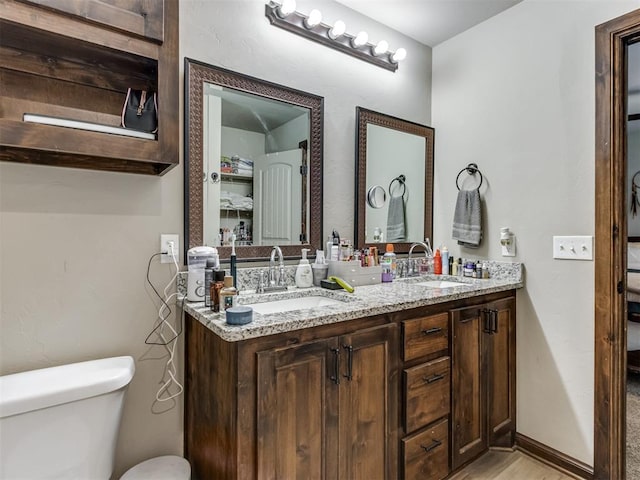 ensuite bathroom with a sink, toilet, double vanity, and wood finished floors
