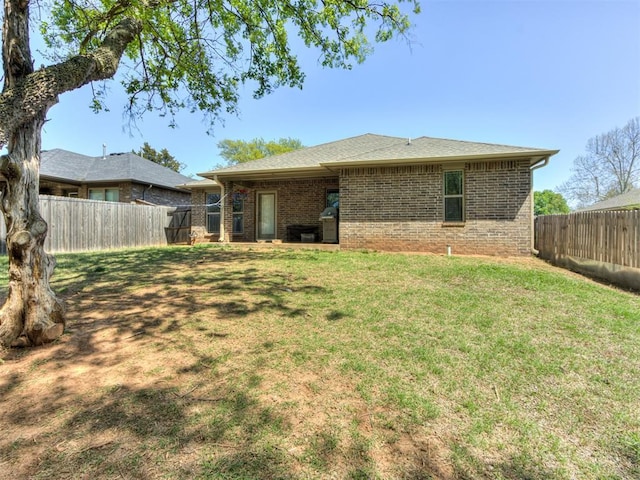 rear view of house featuring a yard, a fenced backyard, and brick siding