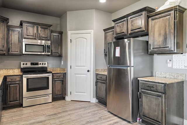 kitchen with light wood-style flooring, appliances with stainless steel finishes, dark brown cabinets, and light stone countertops