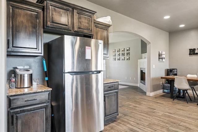 kitchen with recessed lighting, a fireplace, freestanding refrigerator, dark brown cabinets, and arched walkways