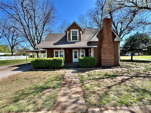 view of front of house featuring a carport, a porch, a chimney, and a front lawn