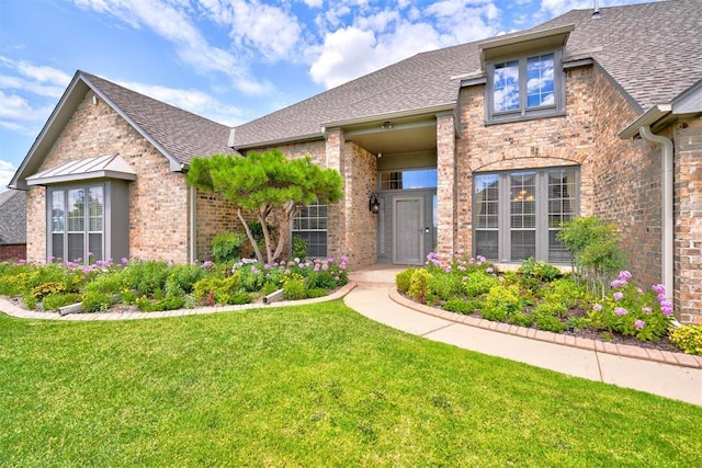 view of front of house featuring brick siding, a shingled roof, and a front lawn