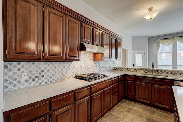 kitchen featuring light countertops, gas stovetop, under cabinet range hood, a sink, and backsplash