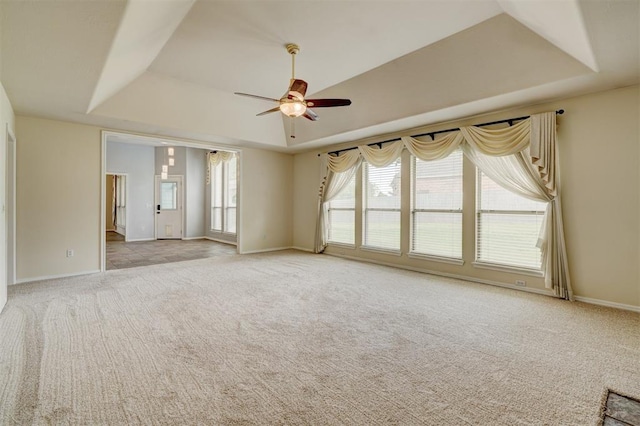 spare room with baseboards, a ceiling fan, a tray ceiling, and light carpet
