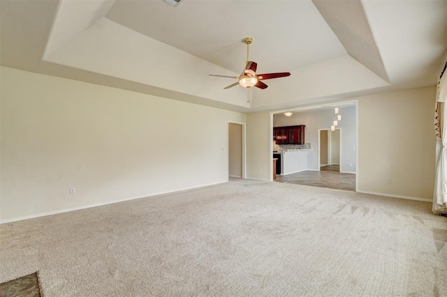 unfurnished living room featuring a ceiling fan, a tray ceiling, light colored carpet, and baseboards