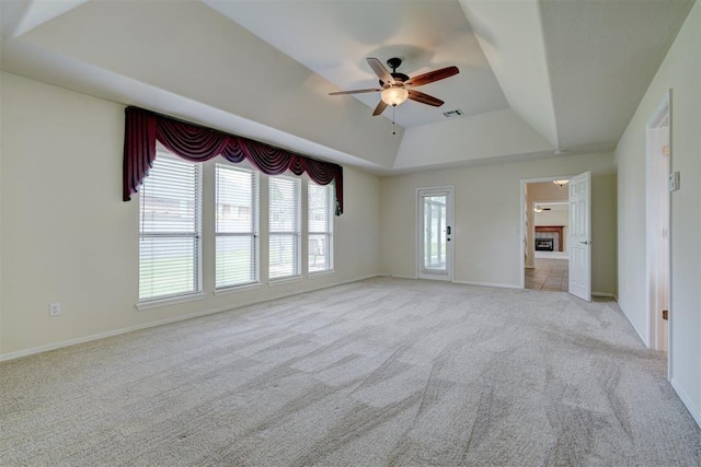 interior space with a raised ceiling, a fireplace, a ceiling fan, baseboards, and visible vents