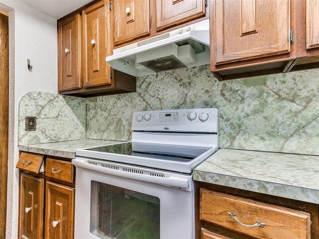 901 Richmond St, Yukon, OK 73099 - kitchen with backsplash, brown cabinetry, electric stove, and under cabinet range hood