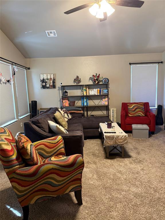 carpeted living area with ceiling fan, lofted ceiling, and visible vents