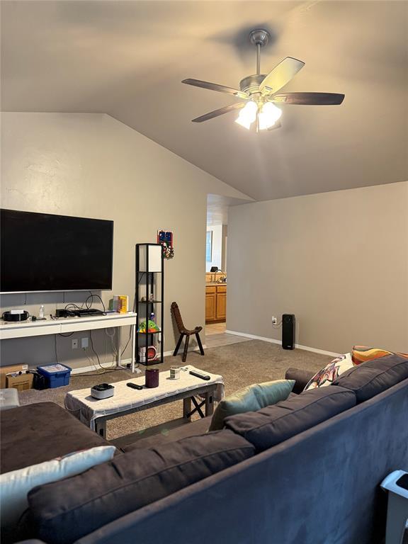 carpeted living area featuring ceiling fan, baseboards, and lofted ceiling