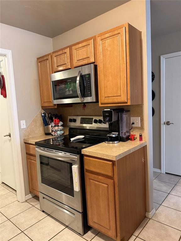 kitchen with brown cabinetry, appliances with stainless steel finishes, light tile patterned floors, and light countertops