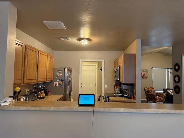 kitchen with brown cabinets, appliances with stainless steel finishes, light countertops, and visible vents