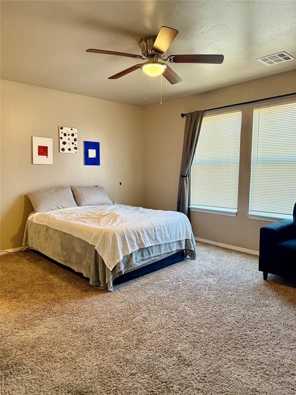carpeted bedroom with baseboards, a ceiling fan, and visible vents