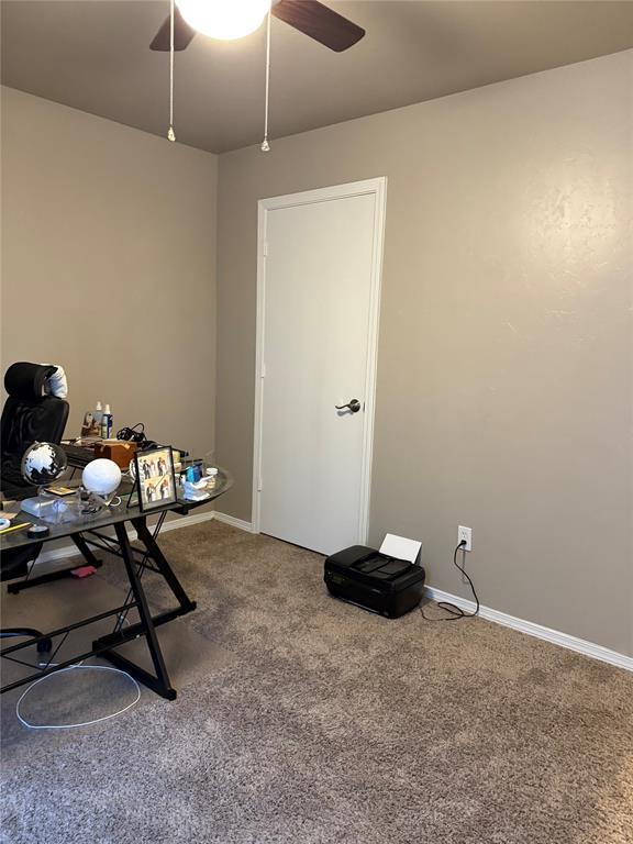 carpeted office space featuring ceiling fan and baseboards