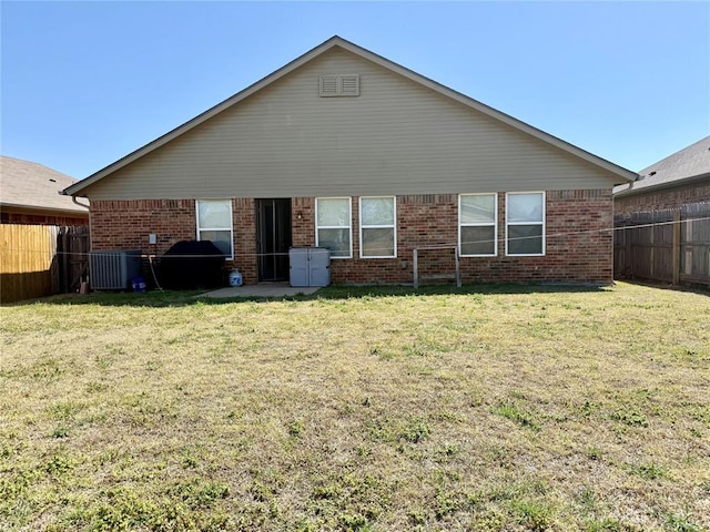 rear view of house with central AC unit, a yard, fence, and brick siding