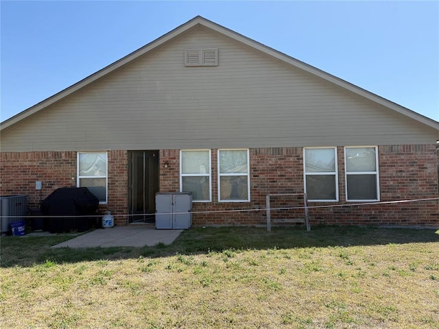 rear view of property with a yard, a patio area, central AC unit, and brick siding