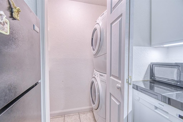 3003 River Oaks Dr Unit 215, Norman, OK 73072 - laundry room featuring stacked washing machine and dryer, a textured wall, light tile patterned floors, and baseboards