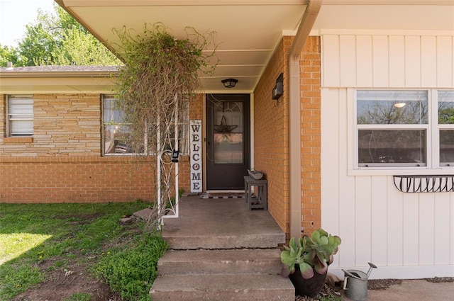 doorway to property featuring board and batten siding and brick siding