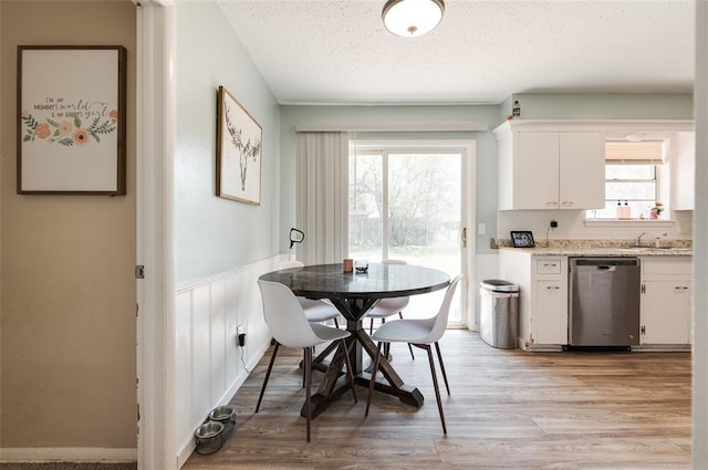 dining space featuring a wainscoted wall, light wood finished floors, and a textured ceiling