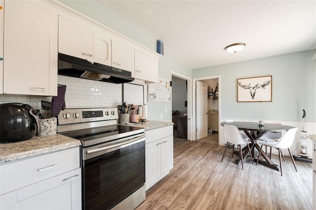 kitchen featuring a textured ceiling, backsplash, stainless steel range with electric stovetop, under cabinet range hood, and light wood finished floors