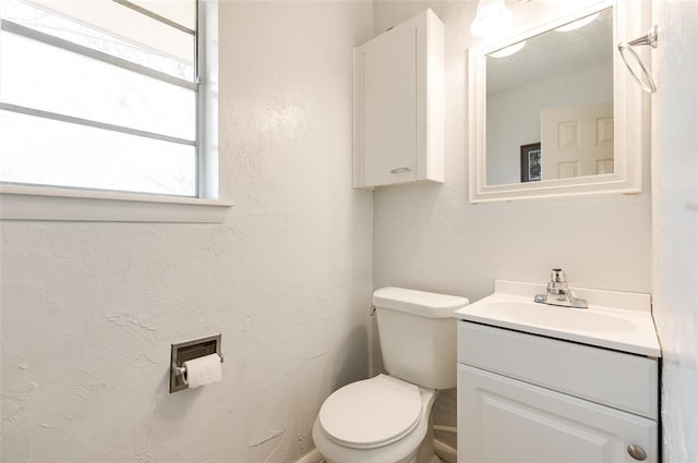 bathroom featuring toilet, vanity, and a textured wall