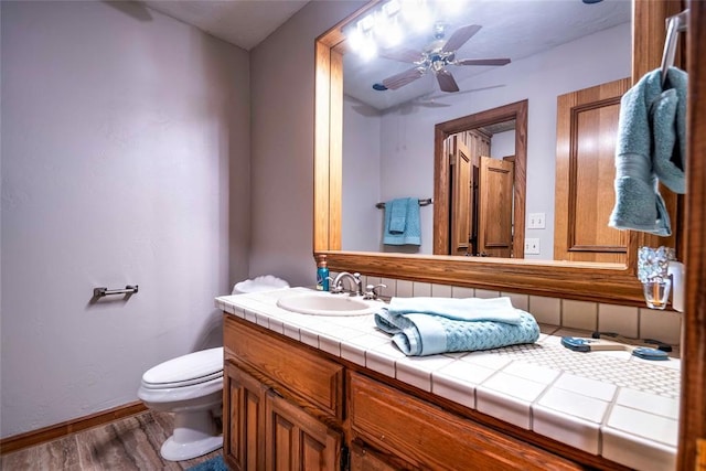 half bath with ceiling fan, vanity, toilet, wood finished floors, and baseboards