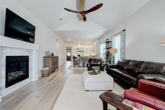 living area featuring high vaulted ceiling, ceiling fan, light wood finished floors, a tiled fireplace, and visible vents
