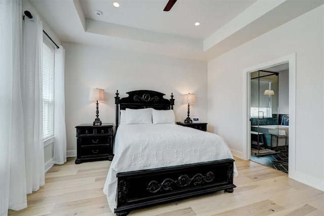 bedroom with recessed lighting, light wood-style flooring, baseboards, and a tray ceiling