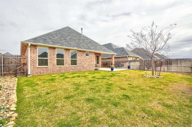 rear view of house featuring brick siding, a yard, a fenced backyard, and a patio