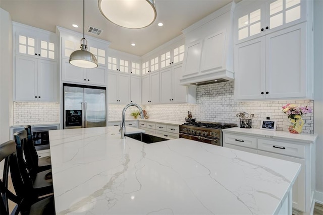 kitchen featuring a sink, a kitchen island with sink, custom range hood, appliances with stainless steel finishes, and visible vents
