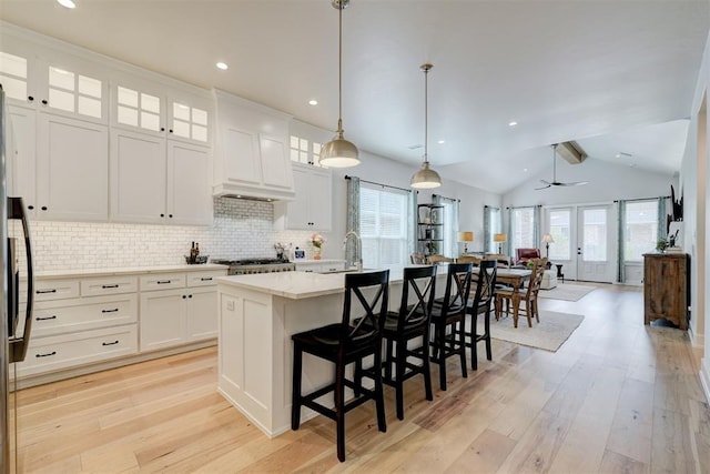 kitchen featuring tasteful backsplash, light wood-style flooring, an island with sink, and custom exhaust hood