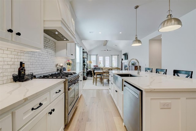 kitchen featuring a sink, tasteful backsplash, vaulted ceiling, appliances with stainless steel finishes, and premium range hood