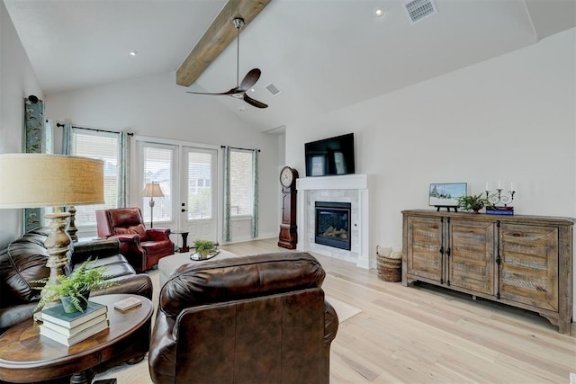 living area featuring a tiled fireplace, vaulted ceiling with beams, visible vents, light wood-style floors, and a ceiling fan
