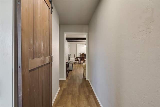 hallway featuring a barn door, dark wood-style flooring, and baseboards