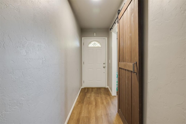 doorway to outside with a textured wall, light wood-style flooring, a barn door, and baseboards