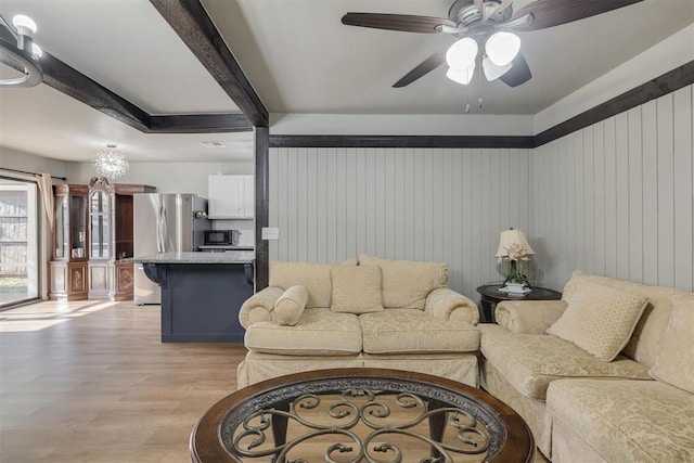 living area featuring wooden walls, beamed ceiling, light wood finished floors, and a ceiling fan