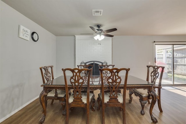dining room featuring a ceiling fan, visible vents, wood finished floors, a brick fireplace, and baseboards
