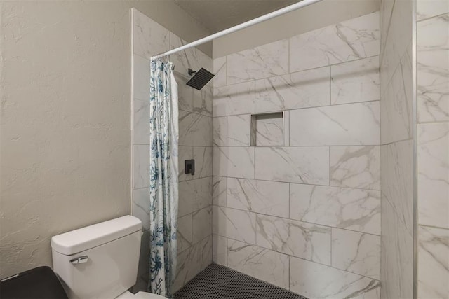 bathroom featuring a textured wall, a tile shower, and toilet
