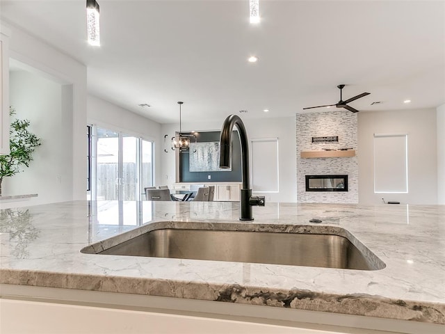 3532 Paso Robles Ter, Edmond, OK 73034 - kitchen featuring decorative light fixtures, a sink, a fireplace, ceiling fan with notable chandelier, and light stone counters