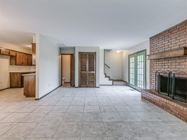 unfurnished living room with french doors, light tile patterned flooring, a brick fireplace, and stairs
