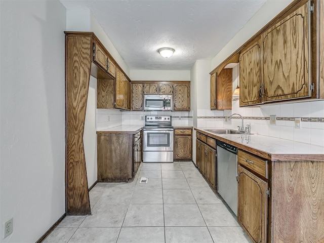 kitchen featuring stainless steel appliances, brown cabinetry, a sink, and backsplash