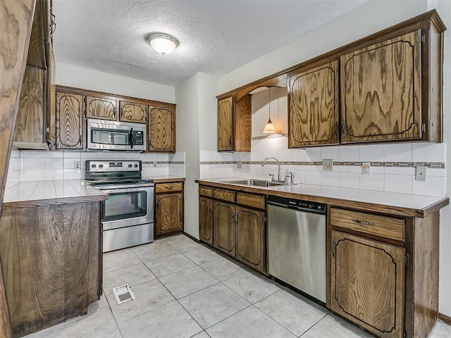 kitchen featuring a textured ceiling, backsplash, appliances with stainless steel finishes, tile countertops, and a sink