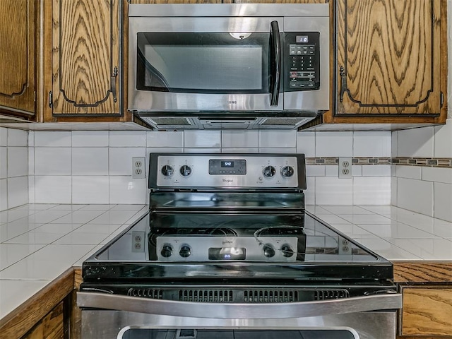 kitchen featuring brown cabinetry, decorative backsplash, appliances with stainless steel finishes, and light countertops