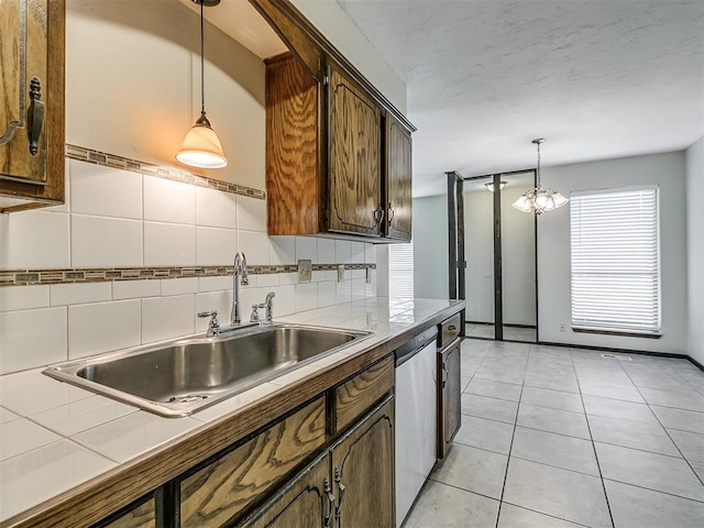 kitchen featuring light tile patterned floors, decorative light fixtures, a sink, tile counters, and stainless steel dishwasher