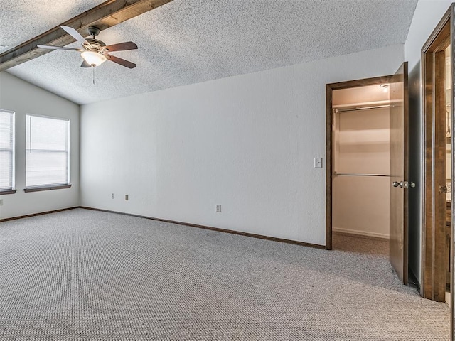 unfurnished bedroom with baseboards, a spacious closet, a textured ceiling, carpet floors, and vaulted ceiling